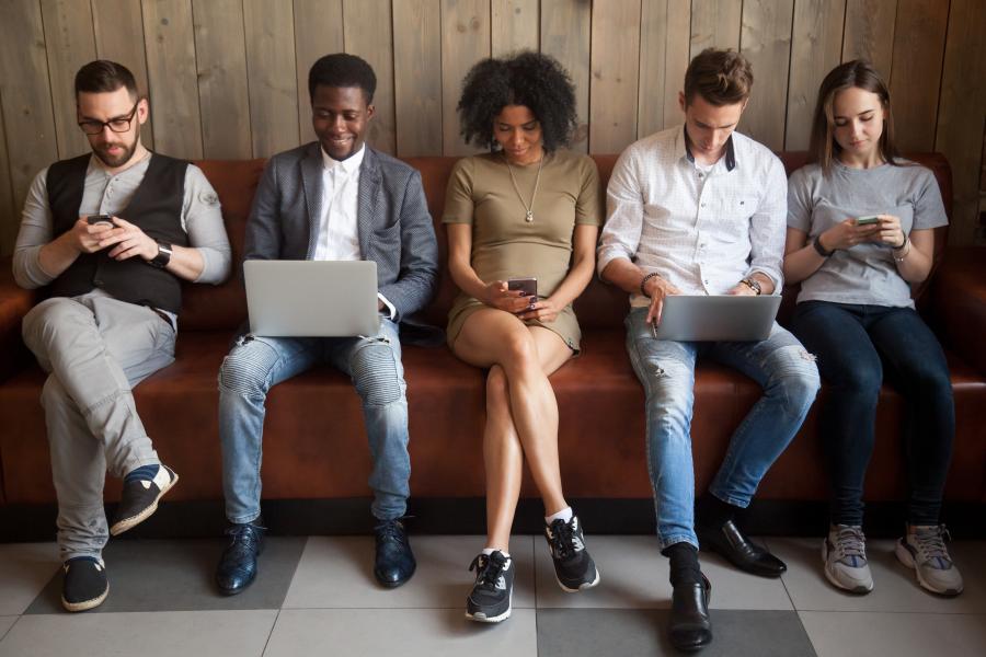 A group of students sitting on a bench using laptops and mobile phones.