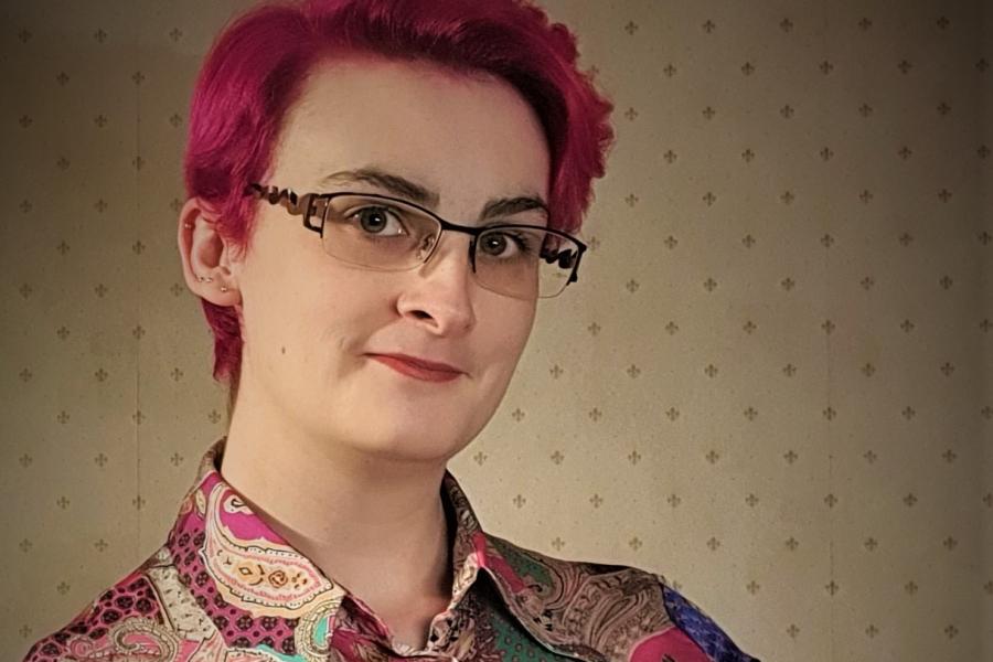 Young woman in a patterned shirt  and wearing spectacles looks into the camera