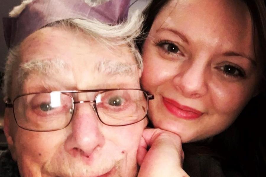 Elderly man looks into camera with young woman behind him