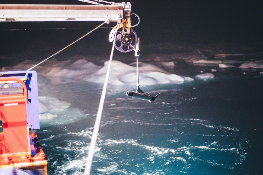A piece iof equipment hangs from the side of a ship above an icy sea