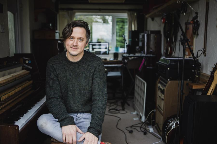 young man loooks into camera sitting in a music studio