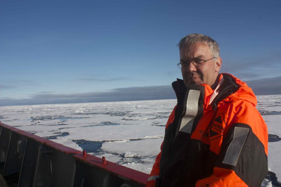 Man on right looks to camera on board a ship, with frozen sea ice in background