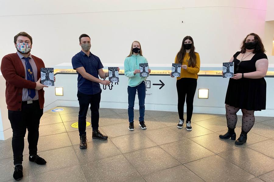 Myfyrwyr Prifysgol Bangor sydd wedi cyhoeddi llyfr a rhai o'r myfyrwyr sydd wedi eu cyhoeddi yn sefyll mewn rhes yn dangos eu llyfr.shed authors stand in a row showing the new publication.