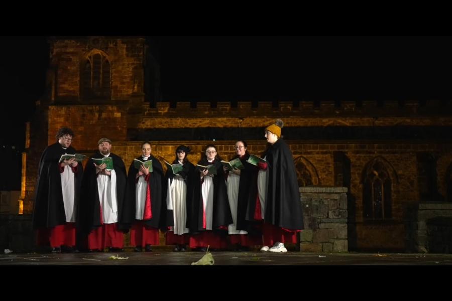 Bangor Cathedral choir perfomr outside Bangor Cathedral at night, as part of Bangor University's festive film