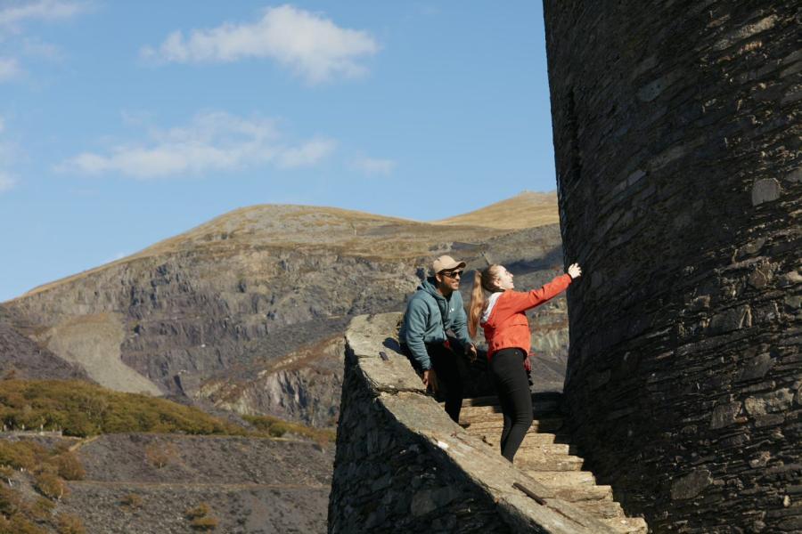 Tirwedd llechi o Lanberis, gyda dau fyfyriwr yn tynnu lluniau