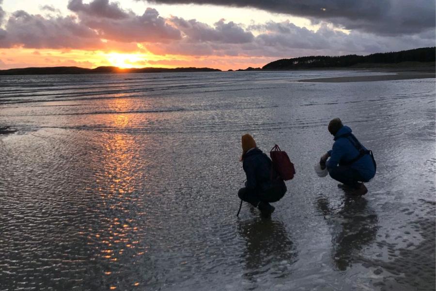 Dau fyfyriwr ar Draeth Llanddwyn fel rhan o hysbyseb teledu Prifysgol Bangor