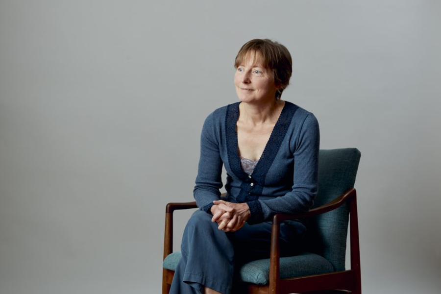 Prof Rebecca Crane sits on a chair in front of grey background