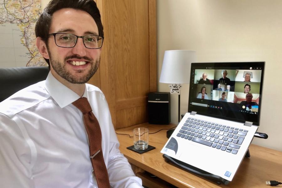 Bespectalced lightly bearded man  and a screen of online participants