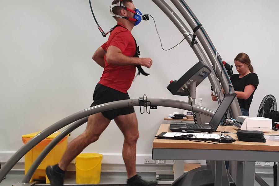 student in a red t-shirt on a treadmill with a mask on his face