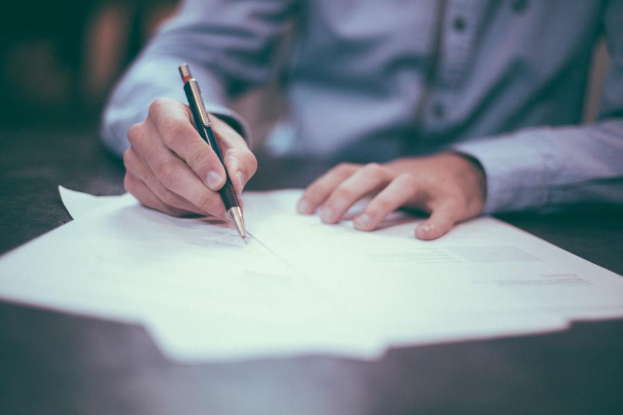 A close up of a man's hands signing a document with a pen