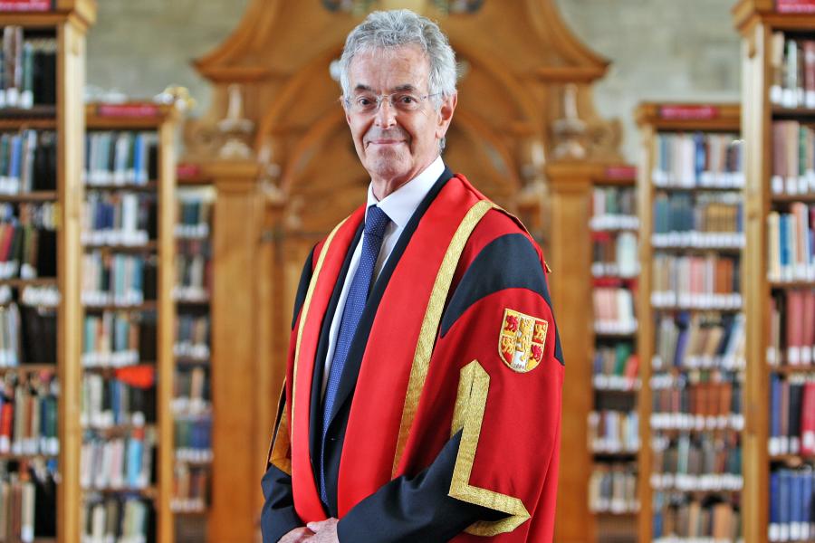 Talll slim man with grey hair and glasses smiles into camera in Bangor University's library.