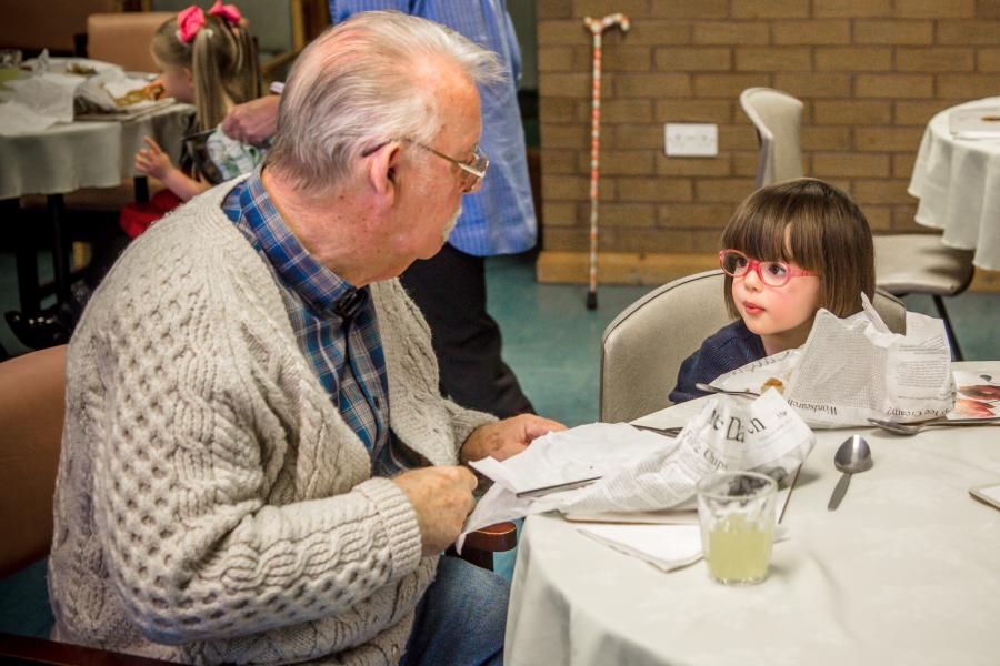 Elderly man sitting at a table with a young child eating fish and chips