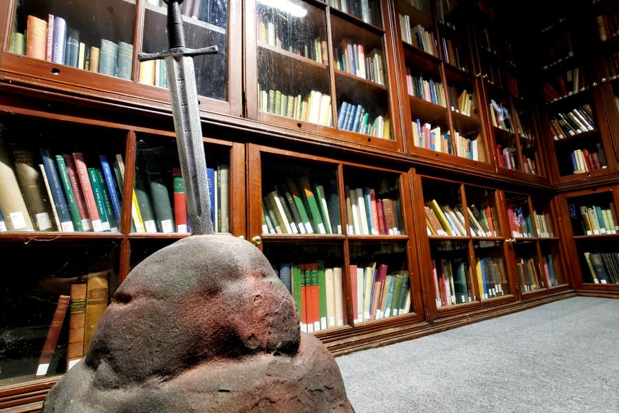 Sword in stone in front of a bookself