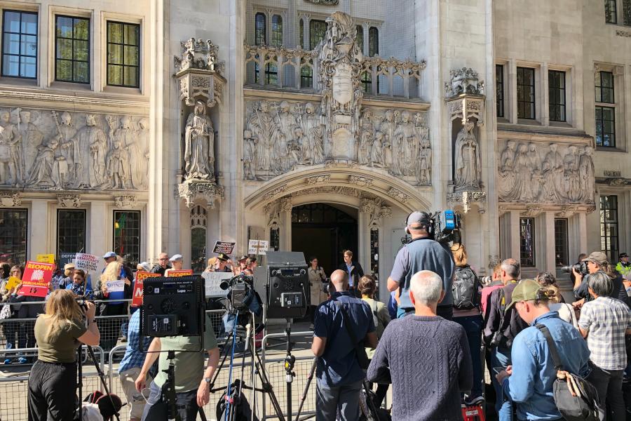 The backof a crowd of media outside an ornate building.