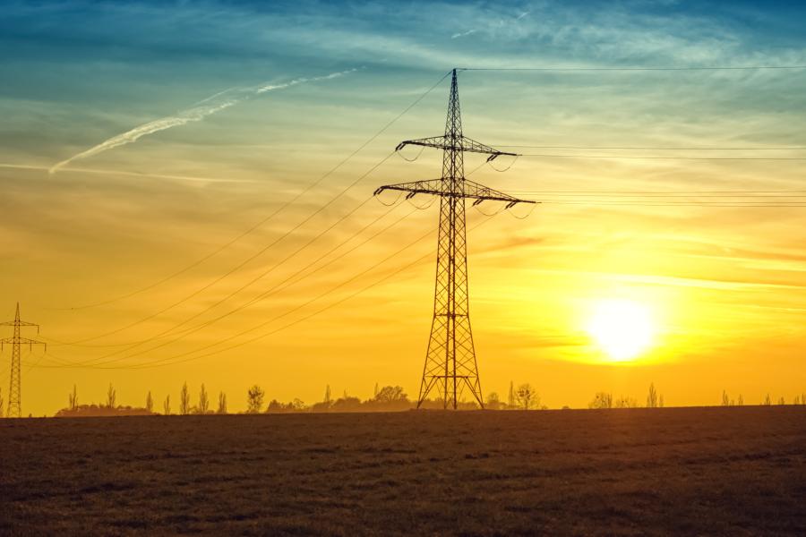 A picture of electricity pylons in a field, against a sunset