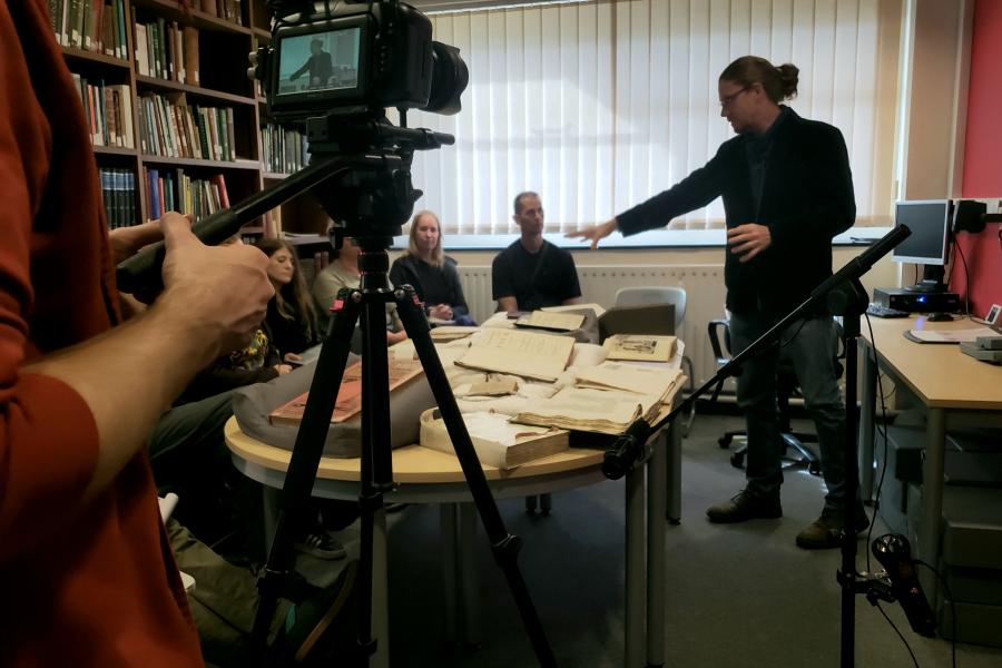 Aled Llion Jones being recorded gesturing at rare books on table