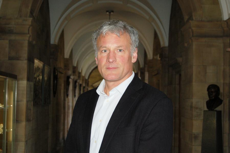 Man stands looking to camera in Bangor University's gothic looking corridor