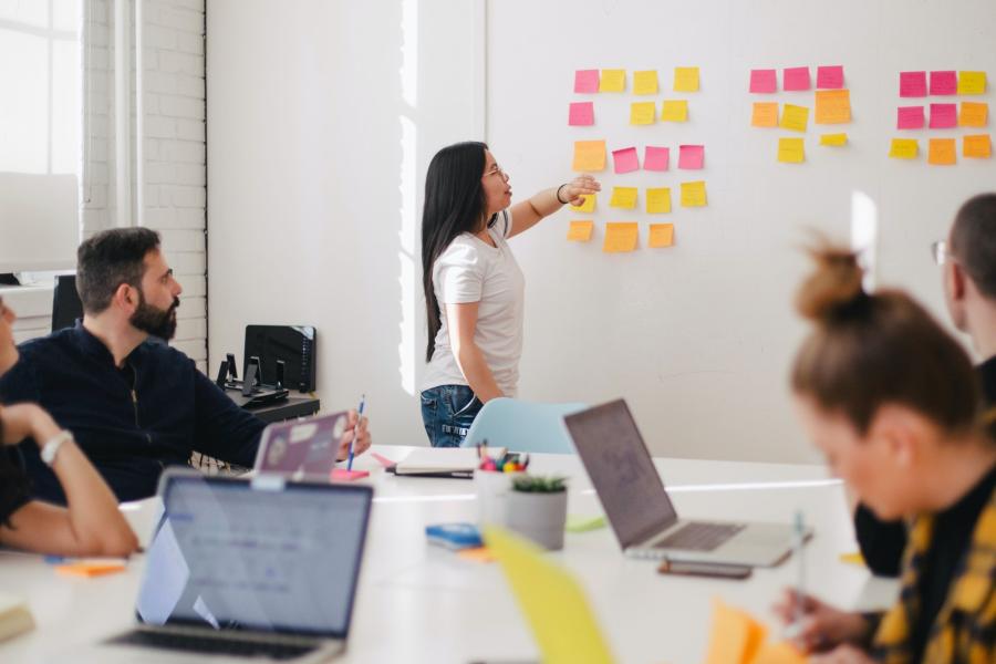 Woman in front of board with sticky notes - room of people- training session