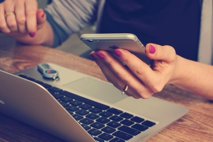 An image of someone working in front of a laptop holding their mobile phone