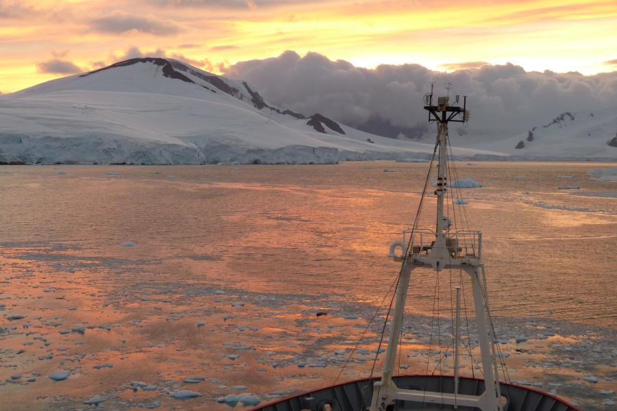 The bow of a ship seen at dawn/ twilight with snowy mountains and glacier ahead.