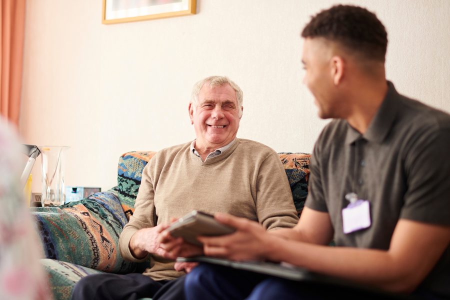 Social Worker smiling at an elderly man, sitting on a sofa