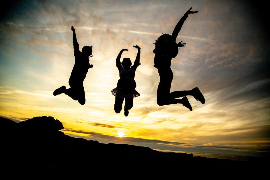 Three people jumping up, with a sunset in the background