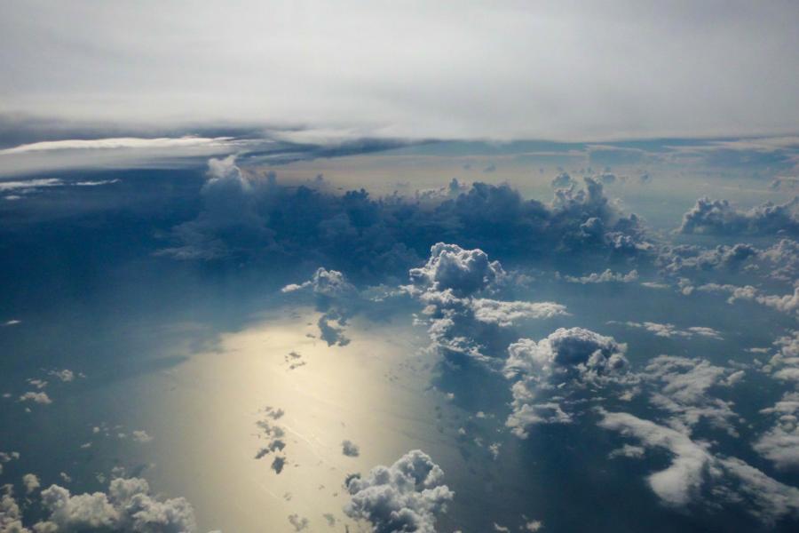 Aerial view looking down at clouds over the sea with sunlight reflected from below