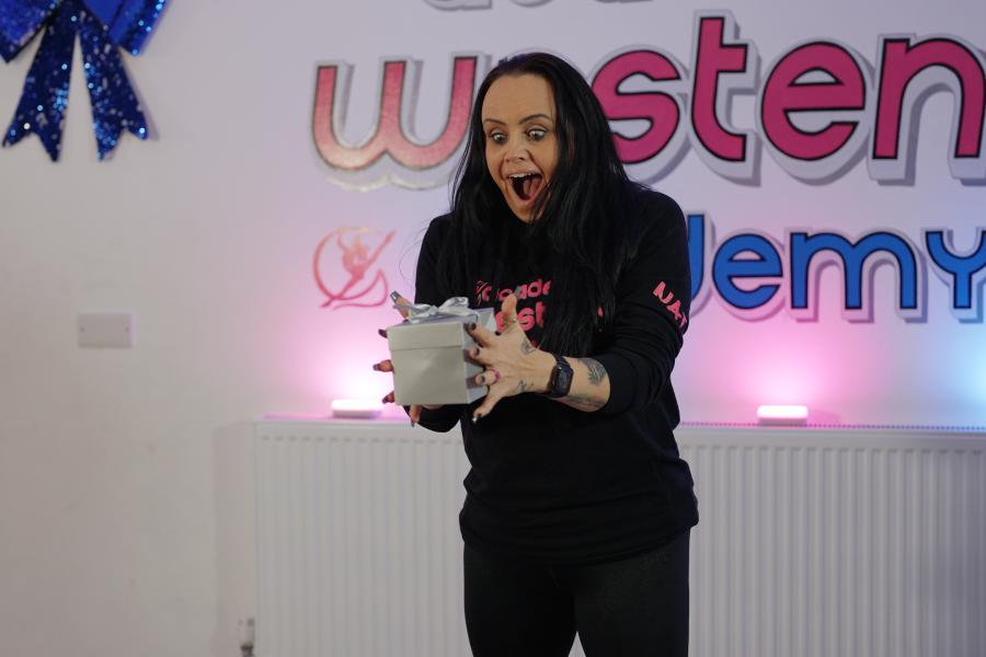 Dance teacher in a class looking surprised as she holds a box 