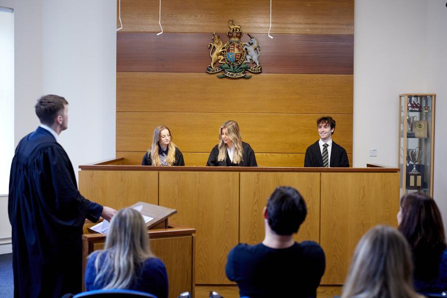 Student brings his case to the mock moot courtroom where three other students act as judges sitting behind the desk in front of audience. 