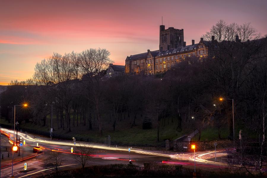 Bangor University's Main Building at dusk with traffic in the foreground and a pink sky in the background