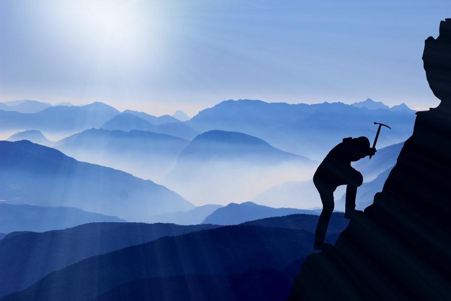 A silhouette of climber wielding an ice pick. In the background are many misty mountain-tops in varying shades of blue