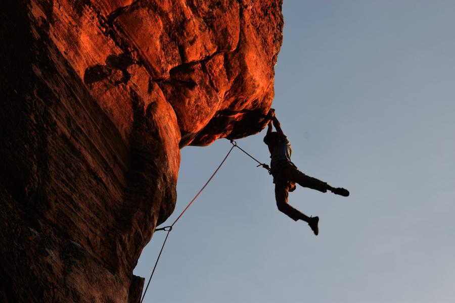 A trad climber hangs by his hands from an overhanging rockface