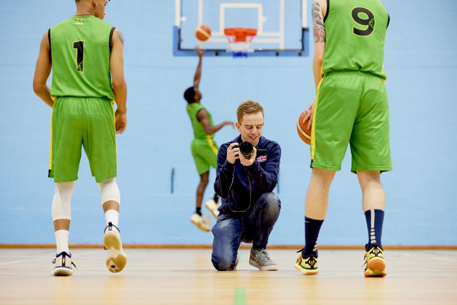 Jamie Thomas, Bangor graduate and social media officer for GB Basketball, on a Basketball court with players from Bangor Badgers Basketball Team