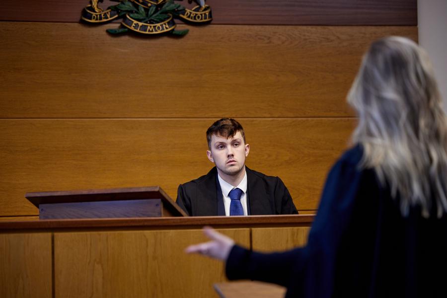 Student sitting behind desk whilst talking to other student practicing mooting in the mock moot court room 