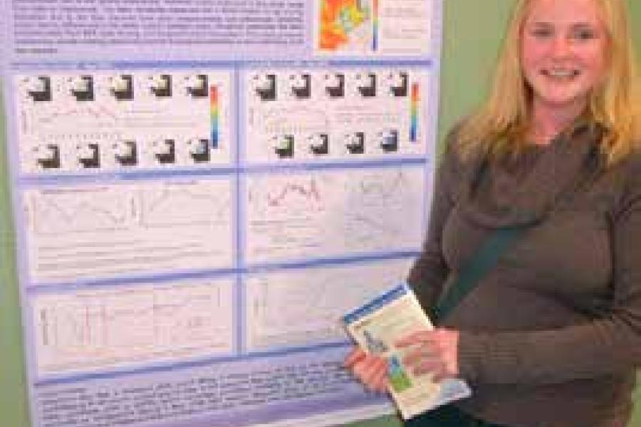 Myfyriwr graddedig, Emmer Litt, yn sefyll o flaen poster ymchwil