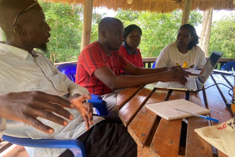 a group of people sitting around a table outside in a hut talking 