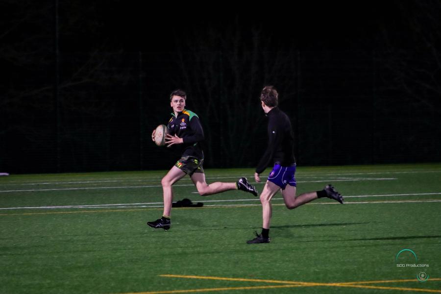 Dau chwaraewr Rygbi'r Undeb. Mae un yn rhedeg efo'r bêl ac yn edrych yn ôl ar un arall sy'n ceisio dal fyny o'r ochr.ith the ball looks back towards the other approaching from the side.