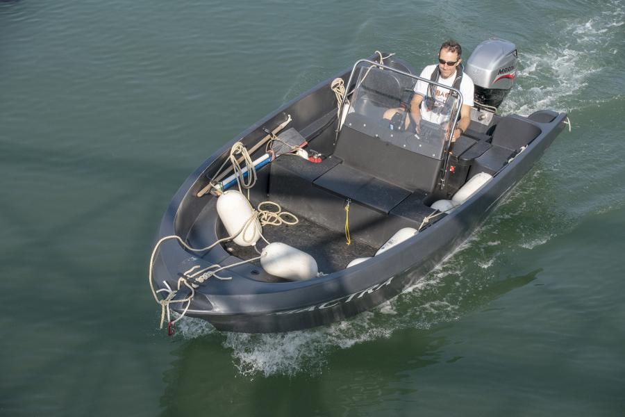 Open grey work boat motoring towards the camera with one person on board