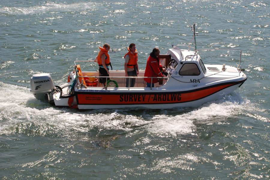 White and orange boat in the sunshine with 3 people on board