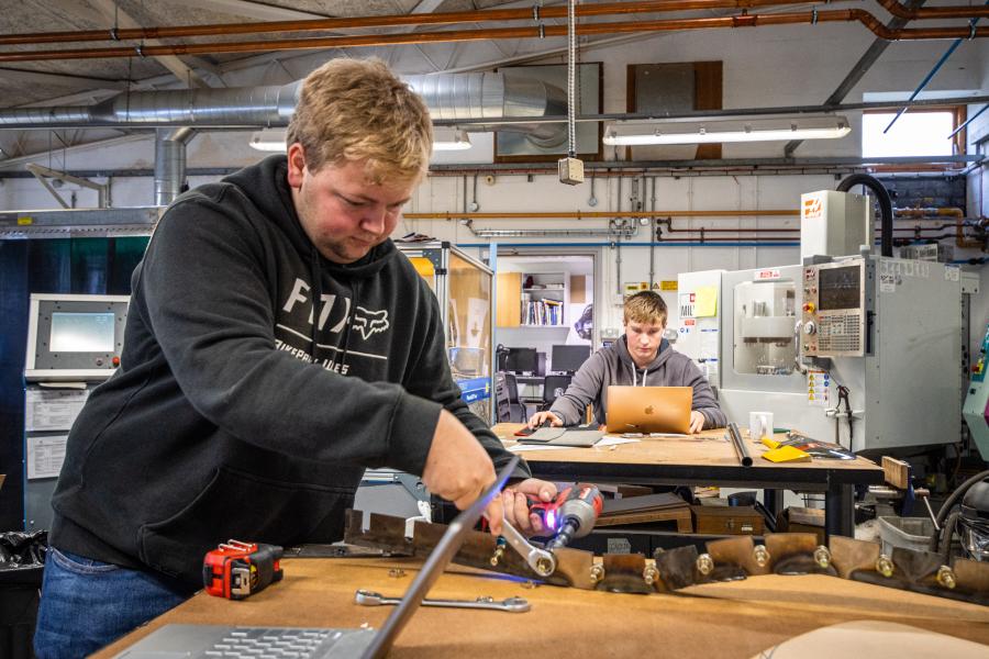 Students in workshop. Near student working on a metal project and far student working on laptop. Hass CNC machine in background