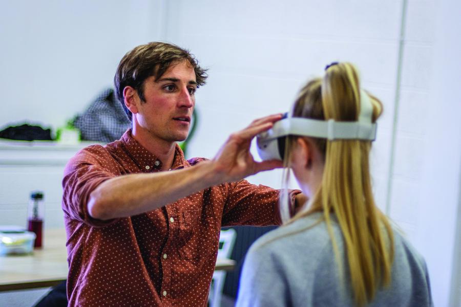 Tim Hunt, Product Design graduate in the workplace, adjusting a VR headset on another person