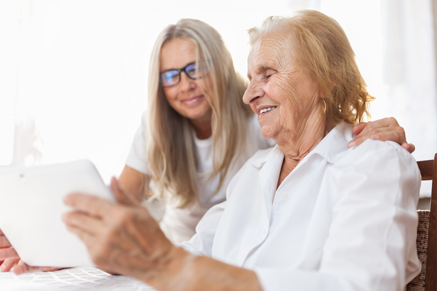 Younger member of family with an elderly member, looking at a tablet screen