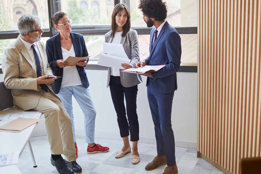 Four people indoors holding papers and talking