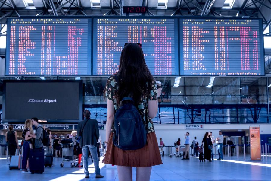 A woman standing in an airport looking at flight times with a backpack on her back