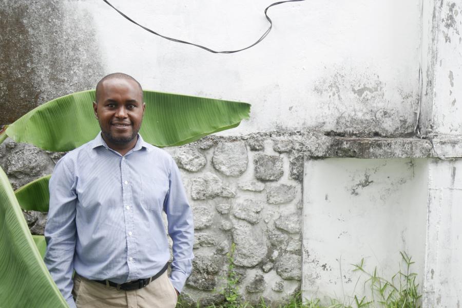 Member of Dahari staff, Misbahou Mohamed standing in front of a whitewashed wall and green plant