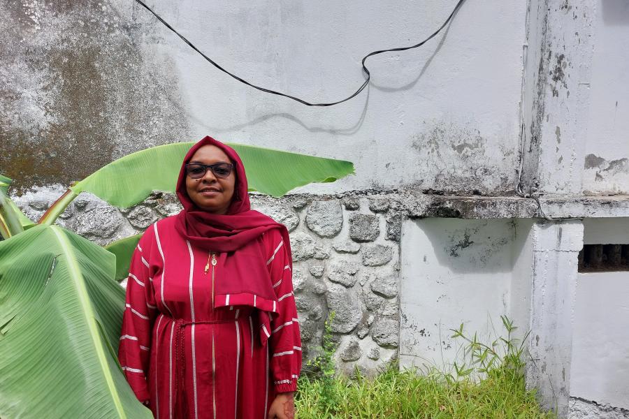 Member of Dahari staff, Siti Mohamed, standing in front of a whitewashed wall and a green plant