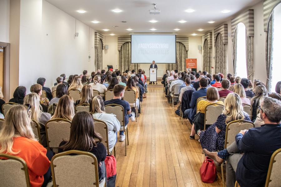 Speaker addresses room full of people whilst making a presentation