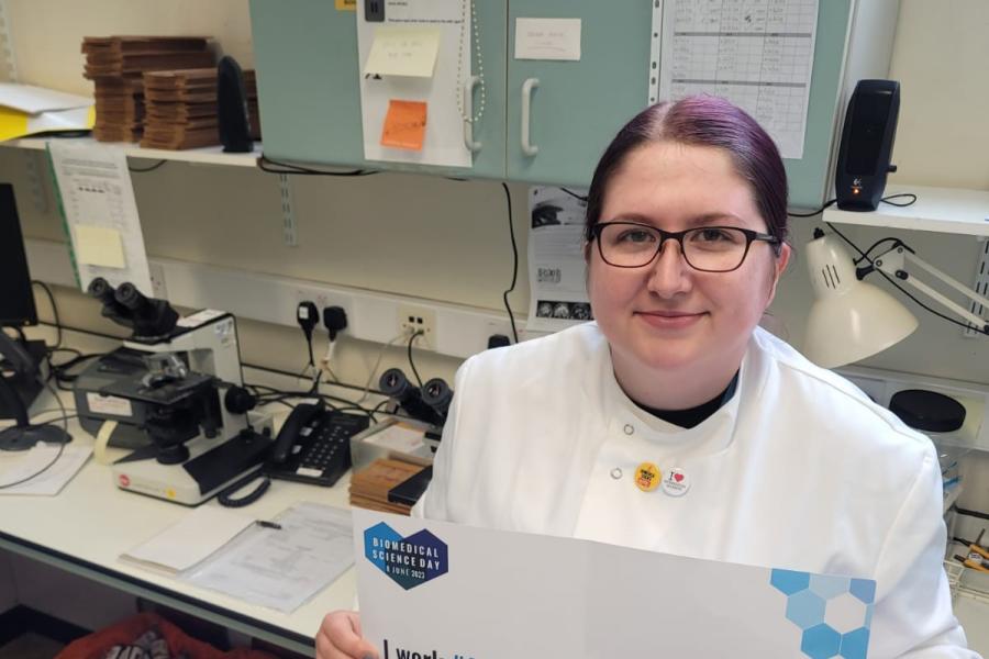 Elisha Hughes in a lab holding a BMS certificate noting that they work as a biomedical scientist