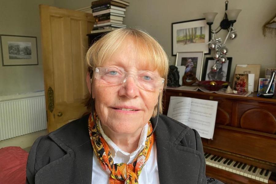Dr Pauline Cutting is sitting in a domestic setting with a piano behind her