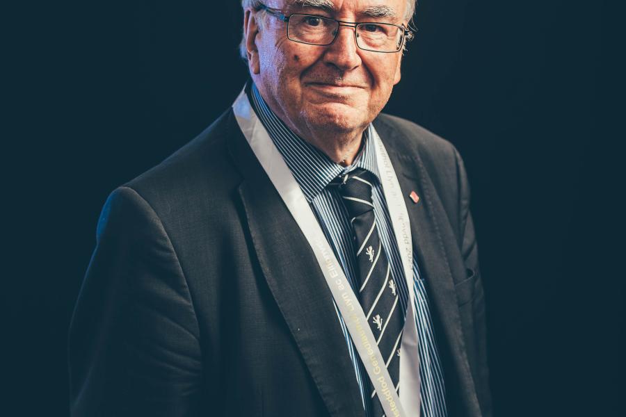 Man against dark background with medal around his neck on a white band.